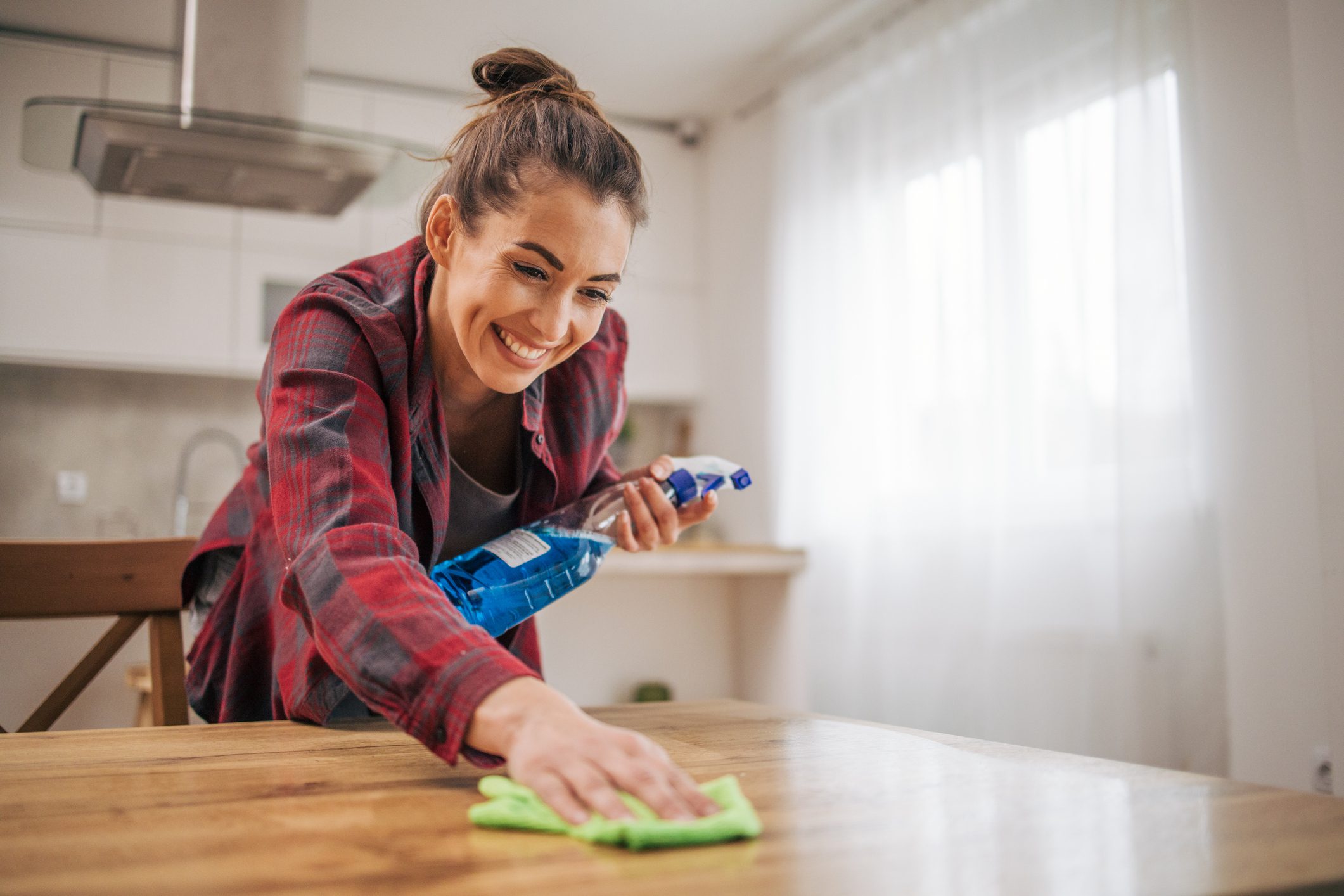 Woman cleaning wooden table with spray bottle.