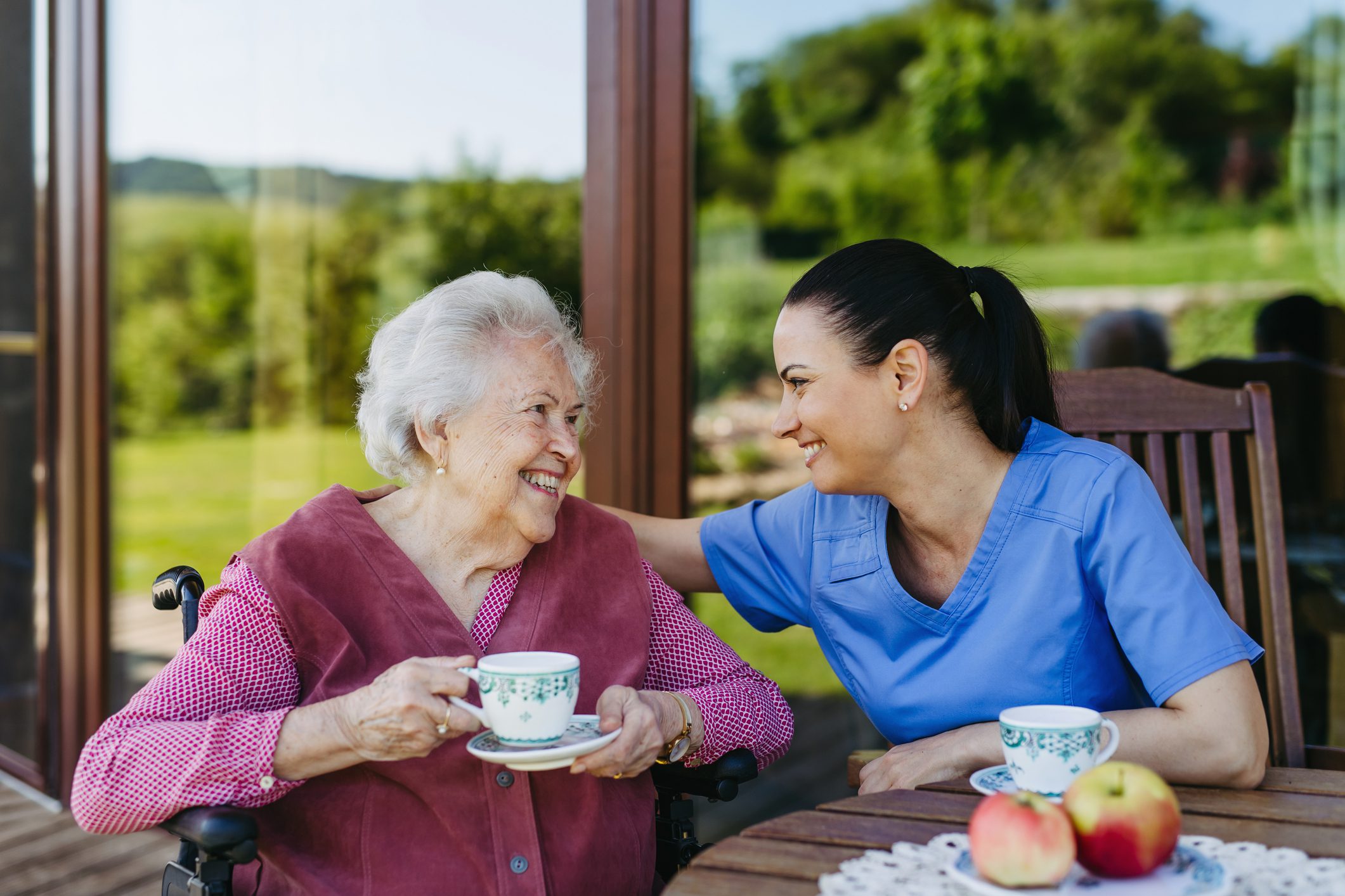 Elderly woman and caregiver enjoying tea outside.