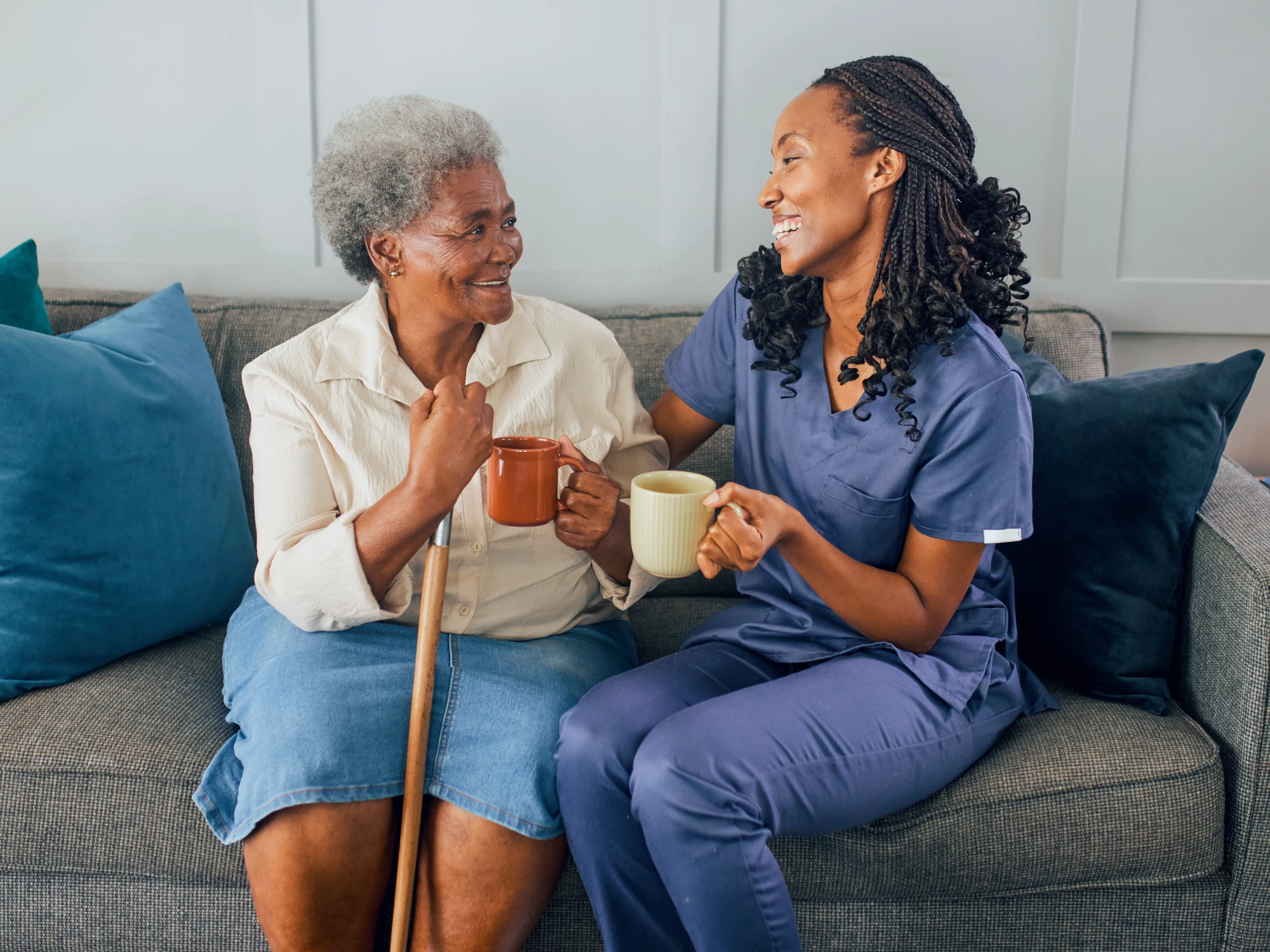 Caregiver enjoying tea with senior on couch, emphasizing structured family caregiving.