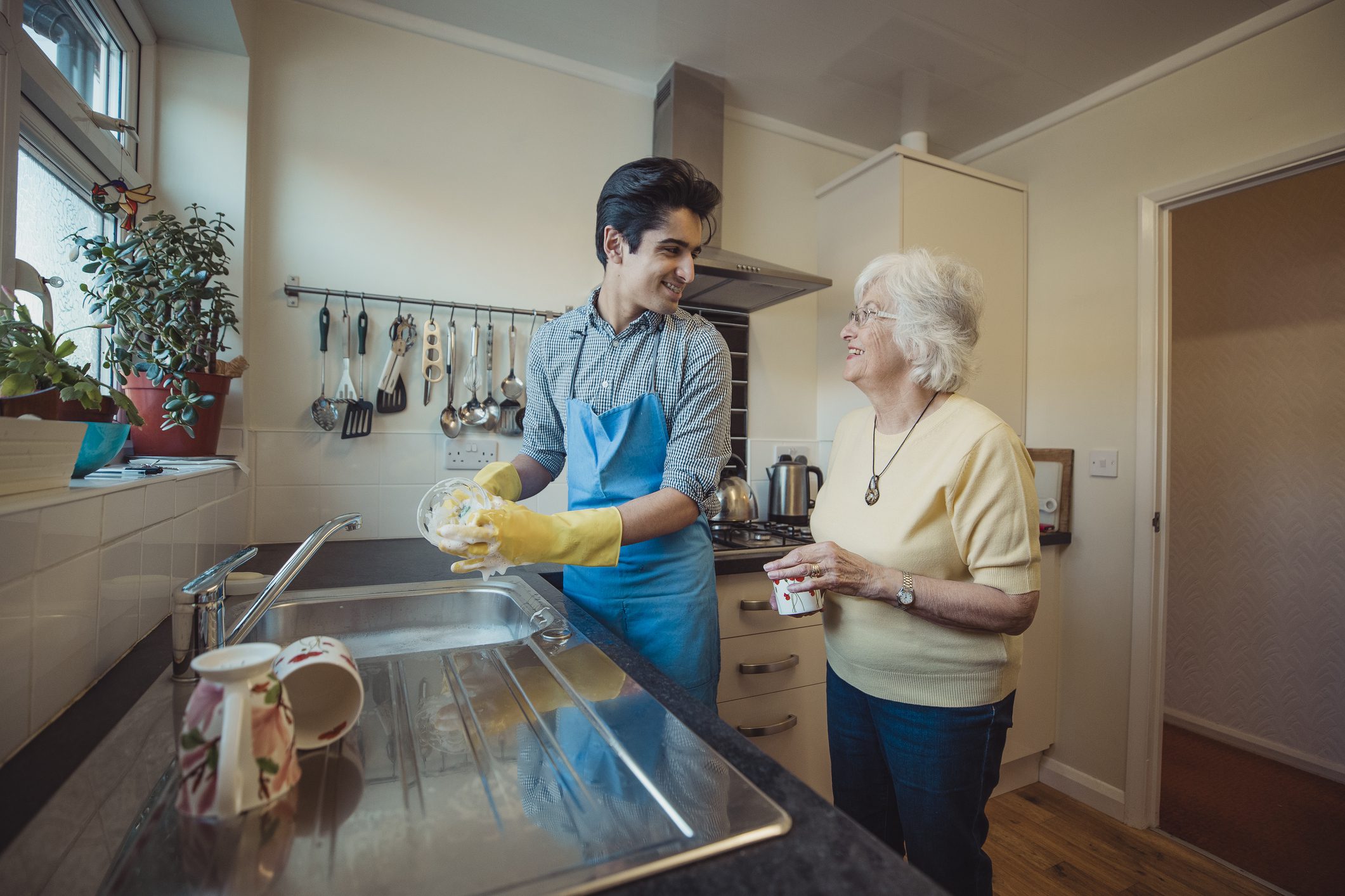 Teenage boy is talking to his grandmother while he washes the dishes in her kitchen.