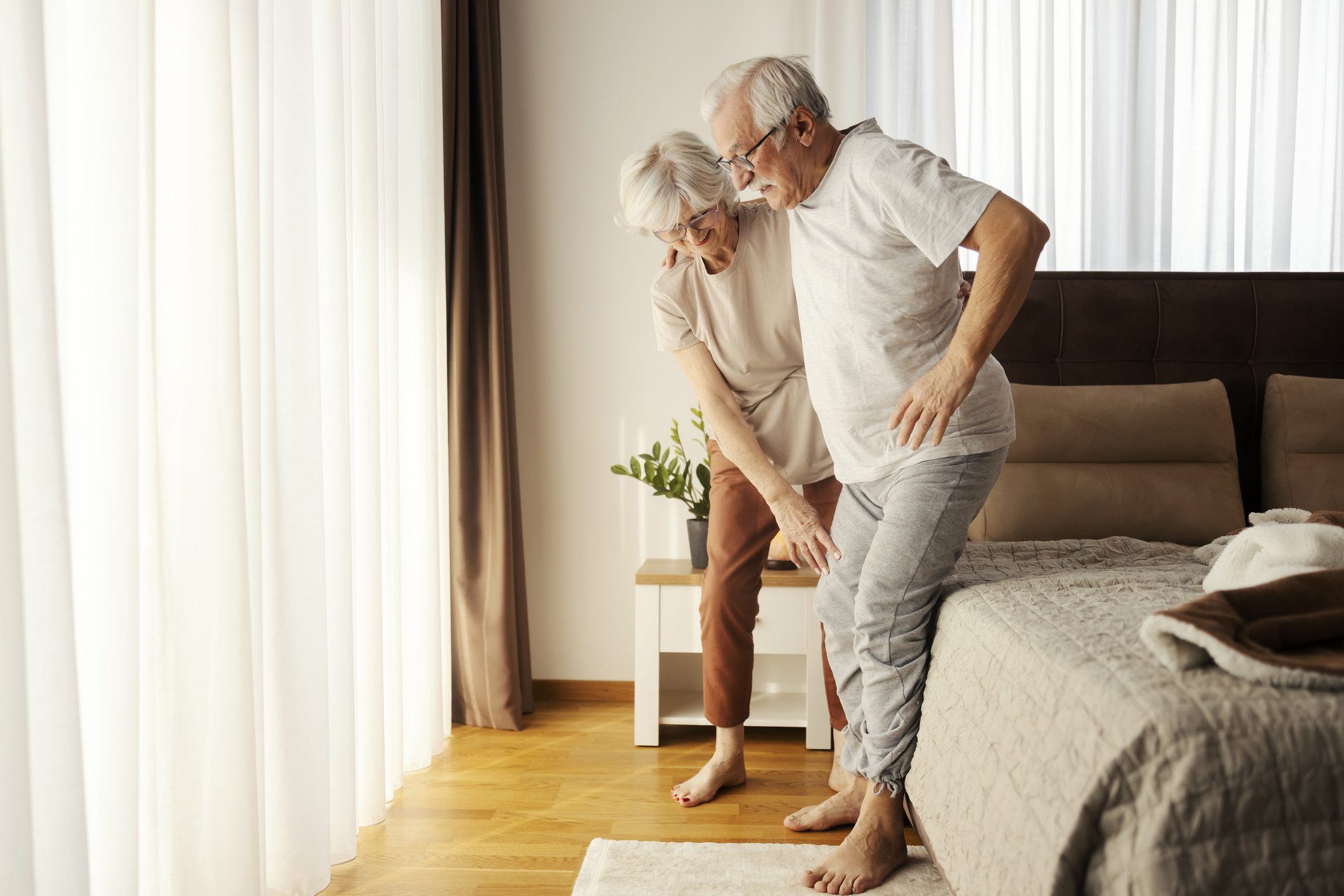 Full length shot of senior woman helping senior man walk from a bed in the morning.